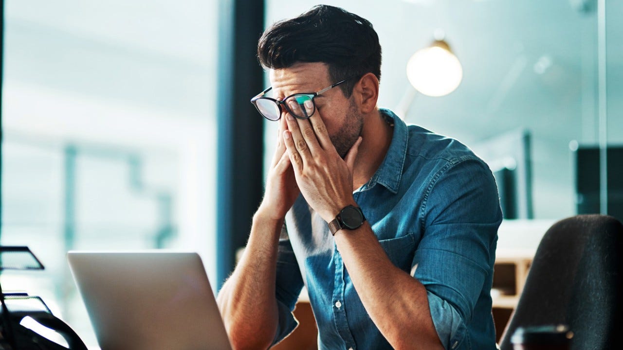 874811642 Shot of a young businessman experiencing stress while using a laptop in a modern office