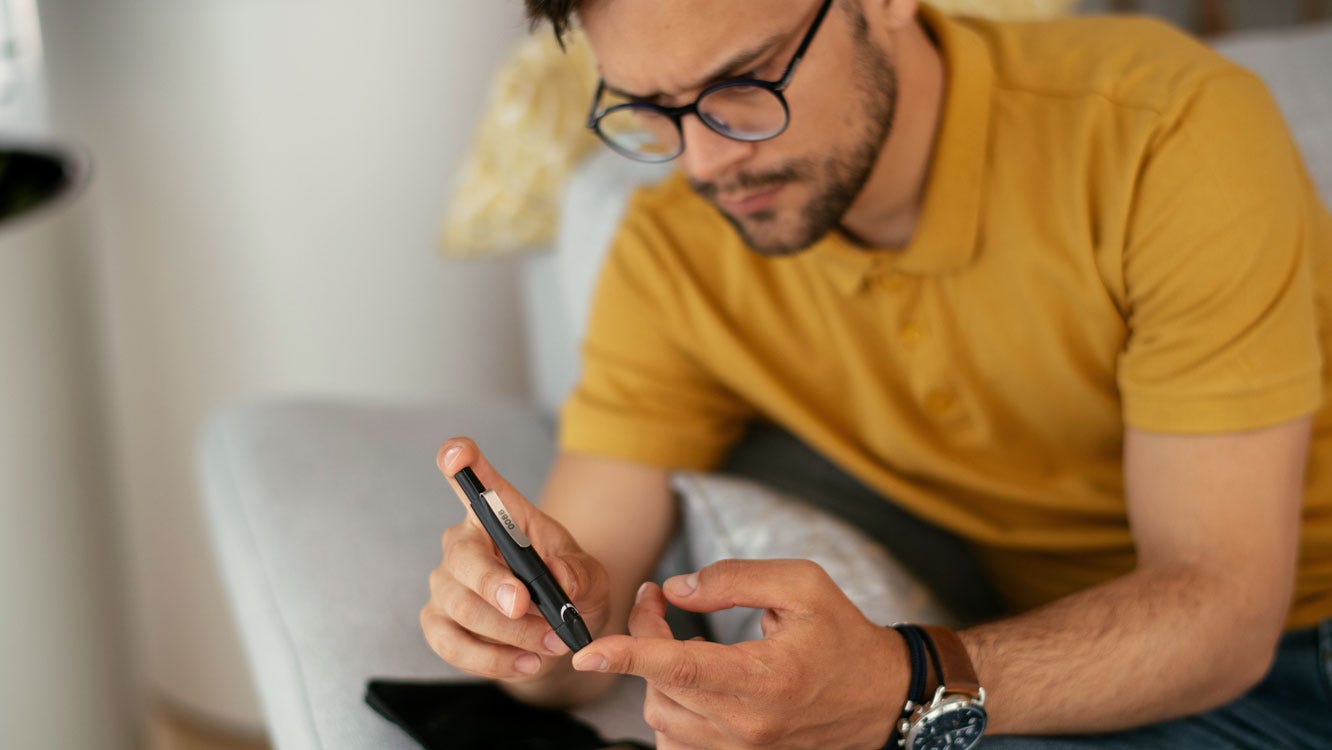 1281255903 Diabetic man taking blood sample with lancet pen at home.