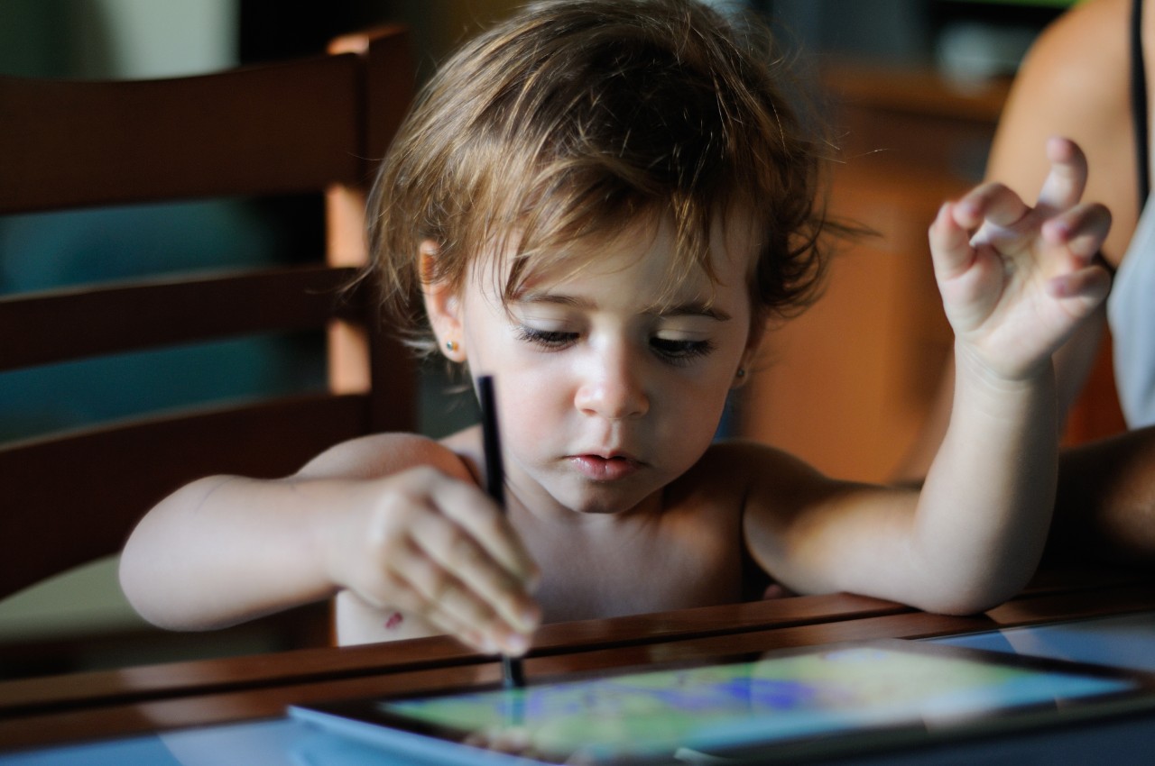 Little girl, two years old, painting with a digital tablet at home.