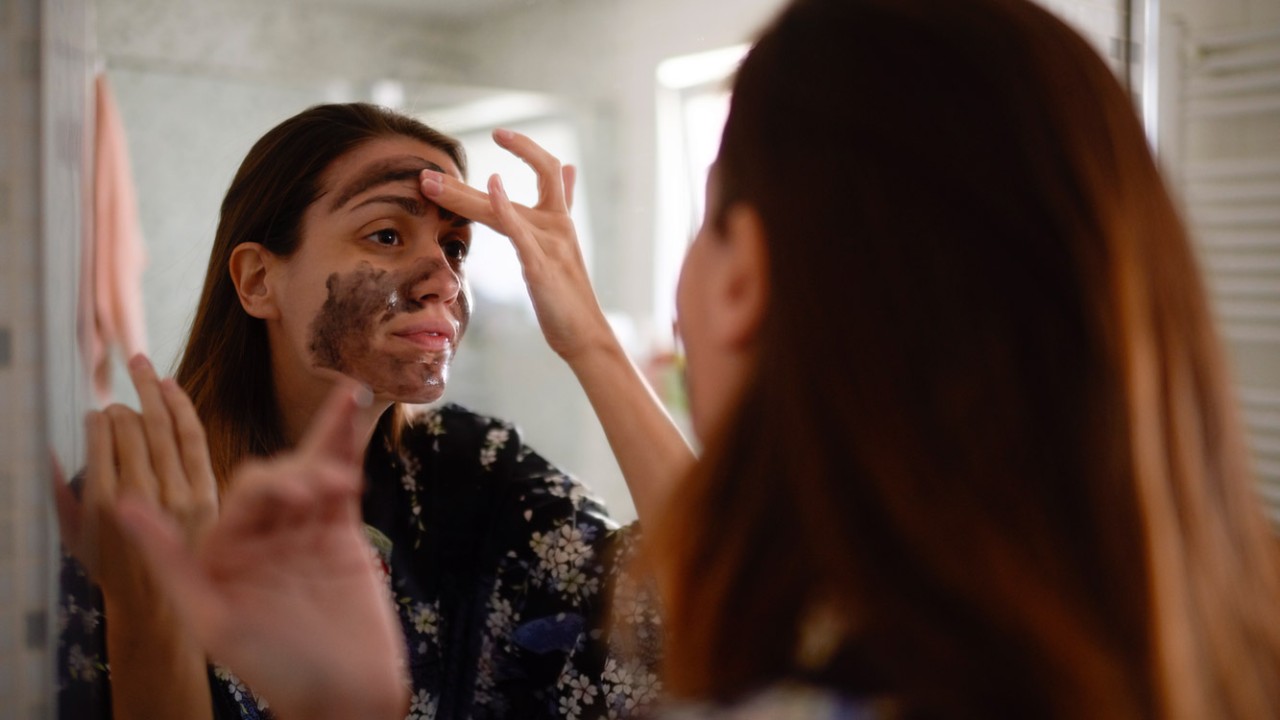 Young female in the bathroom looking in the mirror and taking care of her facial skin.