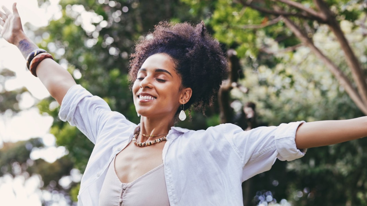 Happy, black woman, smile and freedom for fresh air, relaxation or breathing in the nature outdoors. African American female enjoying holiday vacation, travel or trip with arms out in the forest