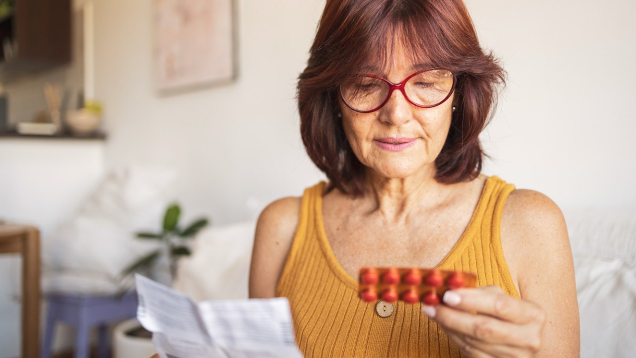 Latin woman using medicine pills. She is sitting on bed and reading patient information leaflet.