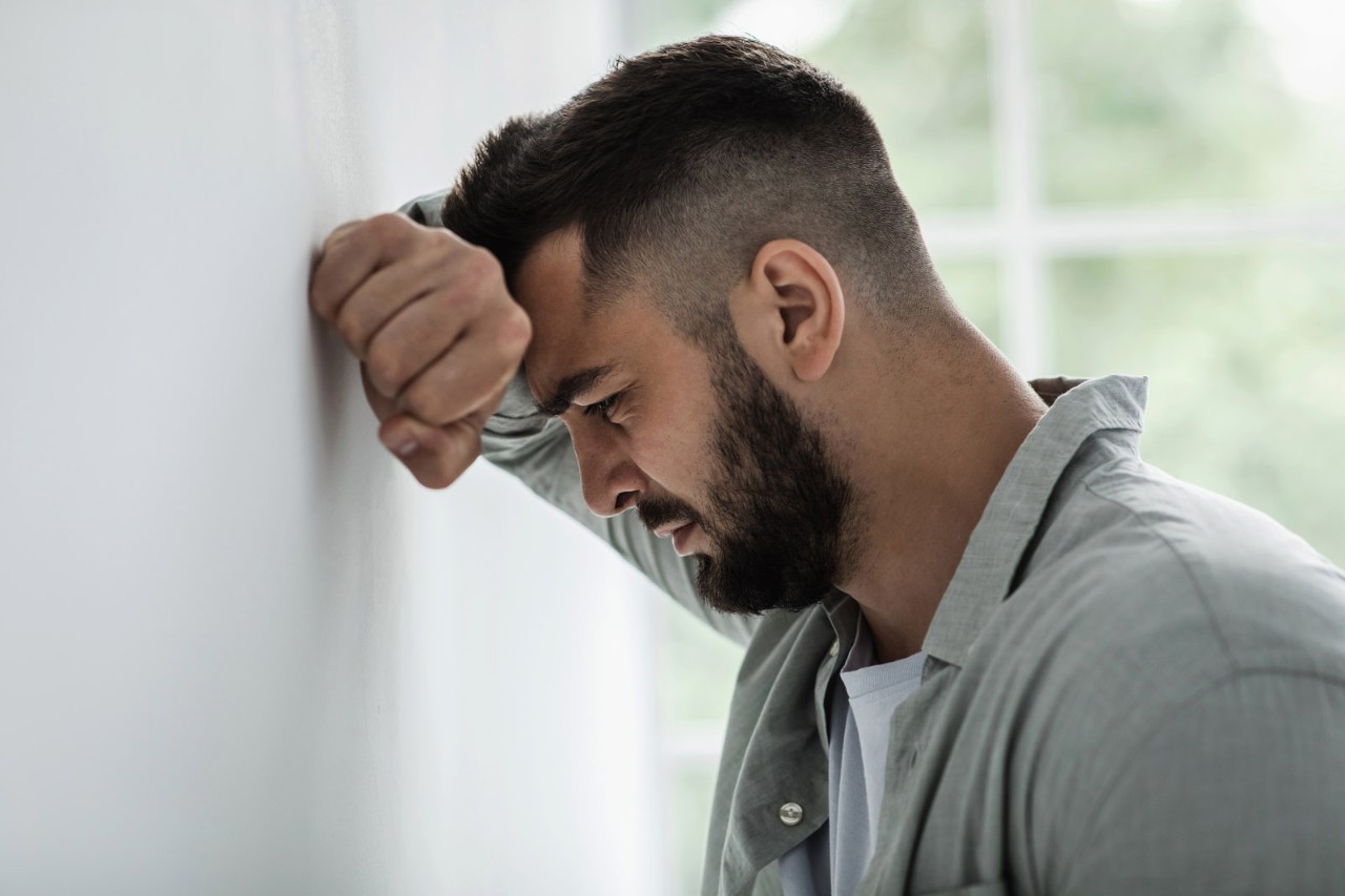 Emotional stress and unhappy, despair, grief and negative emotions, anxiety and agoraphobia. Sad millennial attractive bearded guy resting hand on gray wall and crying, suffer from pain and problems